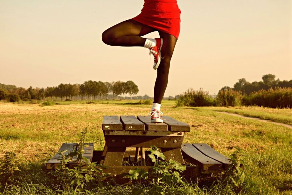 A woman in red balancing on one leg on a picnic table