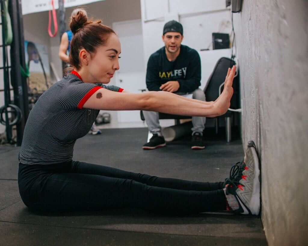 A personal trainer watches his client try a new stretch