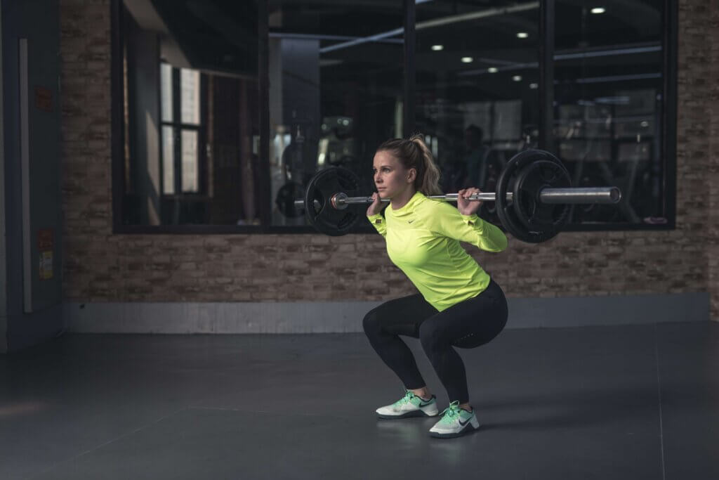 Woman squatting with bar bell over her shoulders.
