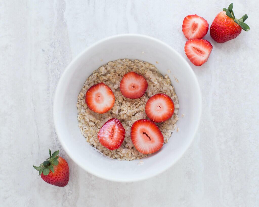 Bowl of plain oatmeal with sliced strawberries on top