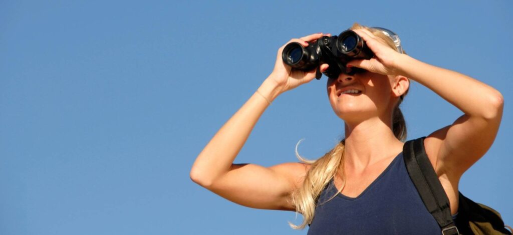 A fit woman outdoors. She is using binoculars to search for her personal trainer in San Francisco